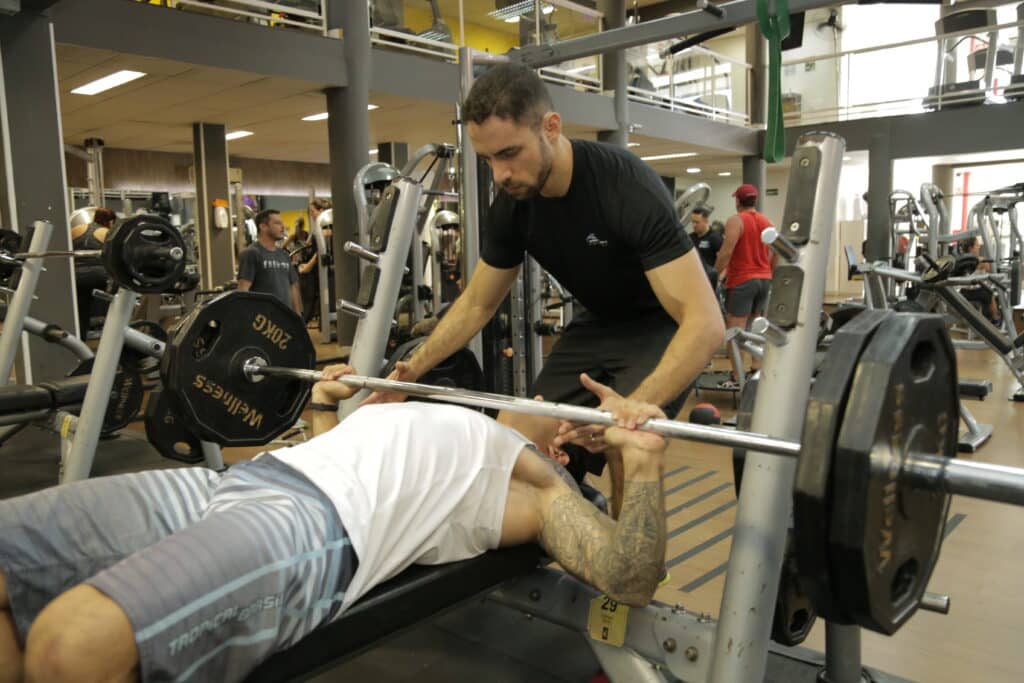 personal trainer com aluno no supino