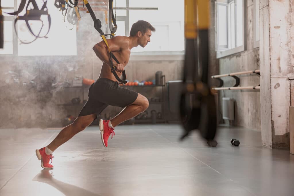 homem treinando com consistência usando trx em uma academia