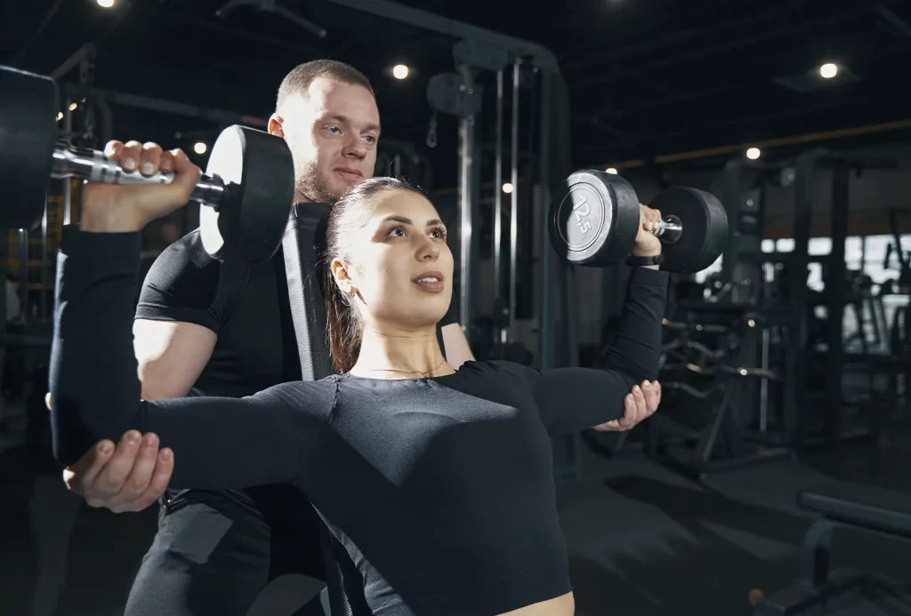 mulher treinando musculação com personal trainer- desenvolvimento de ombros