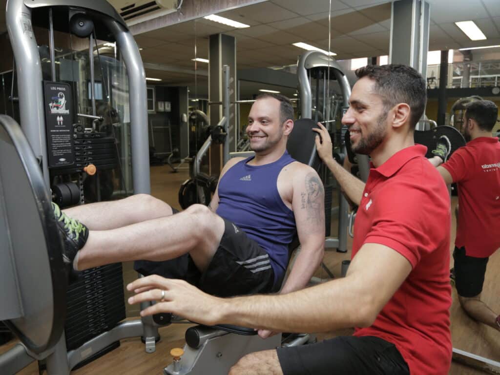 Personal trainer com aluno no leg press