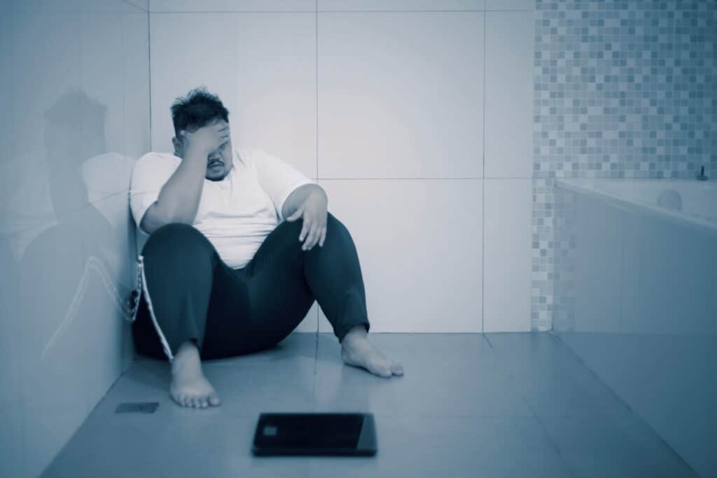 homem triste sentado no banheiro com balança não consegue emagrecer