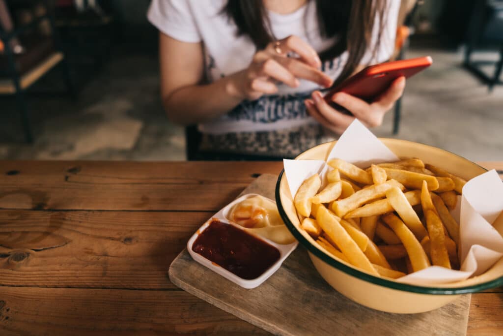 mulher comendo batata frita com smartphone