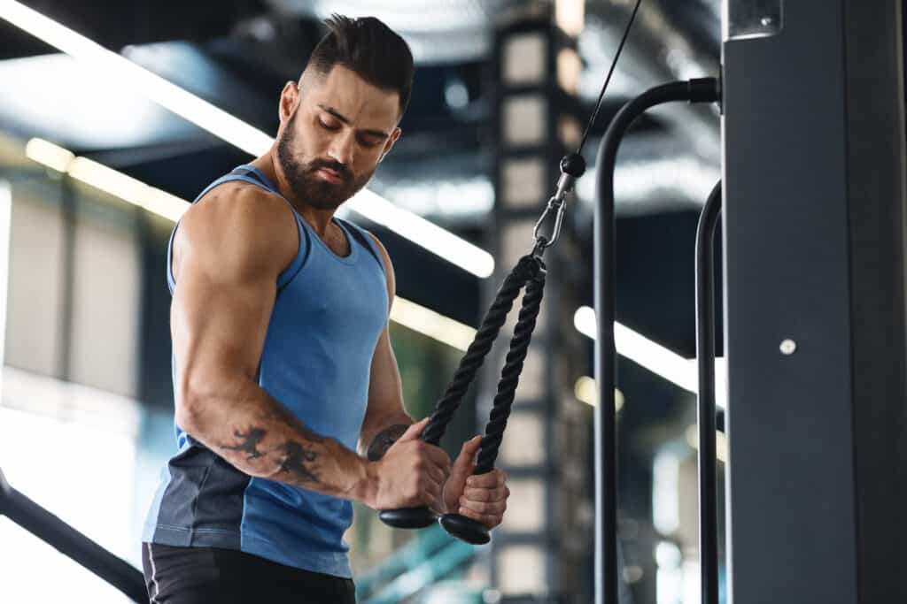 Sport concept. Muscular man exercising with training apparatus in gym, empty space