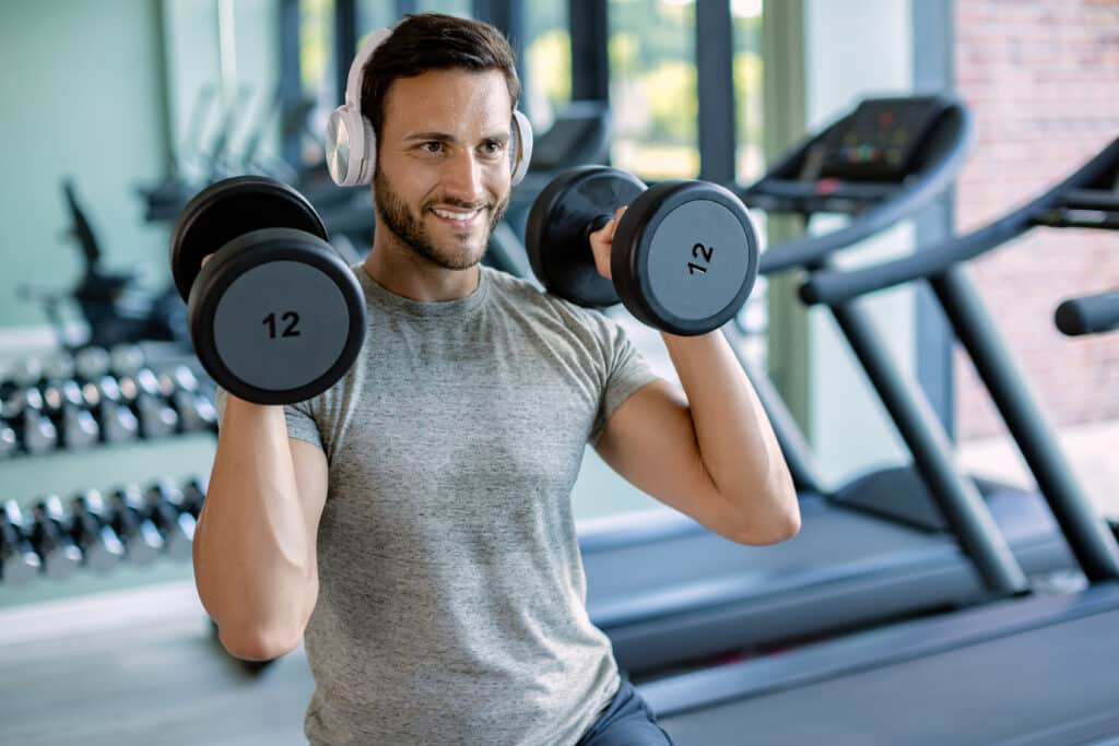 Happy athlete exercising with hand weights during cross training in a gym.